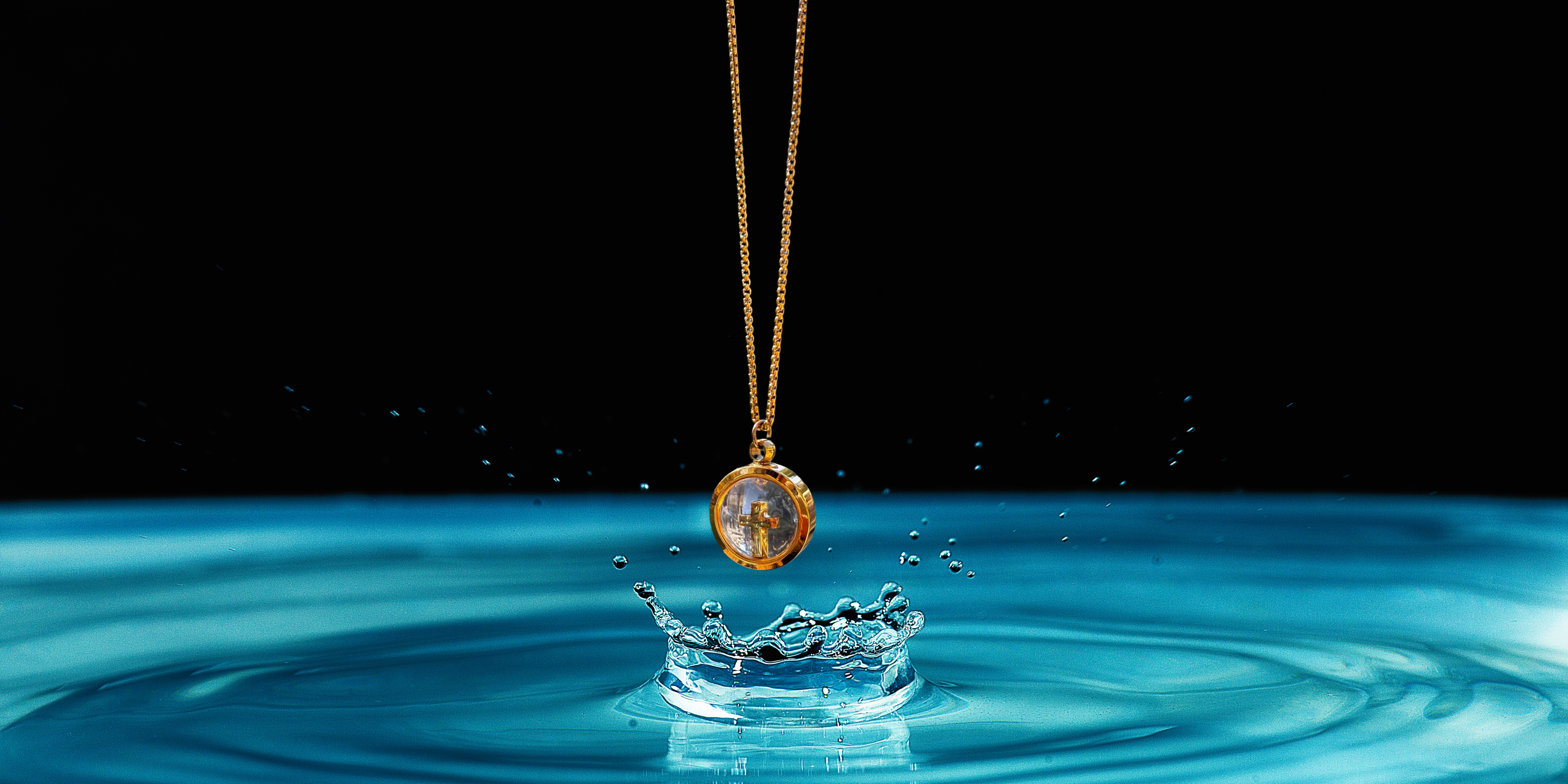 Gold necklace with a pendant splashing into water on a black background